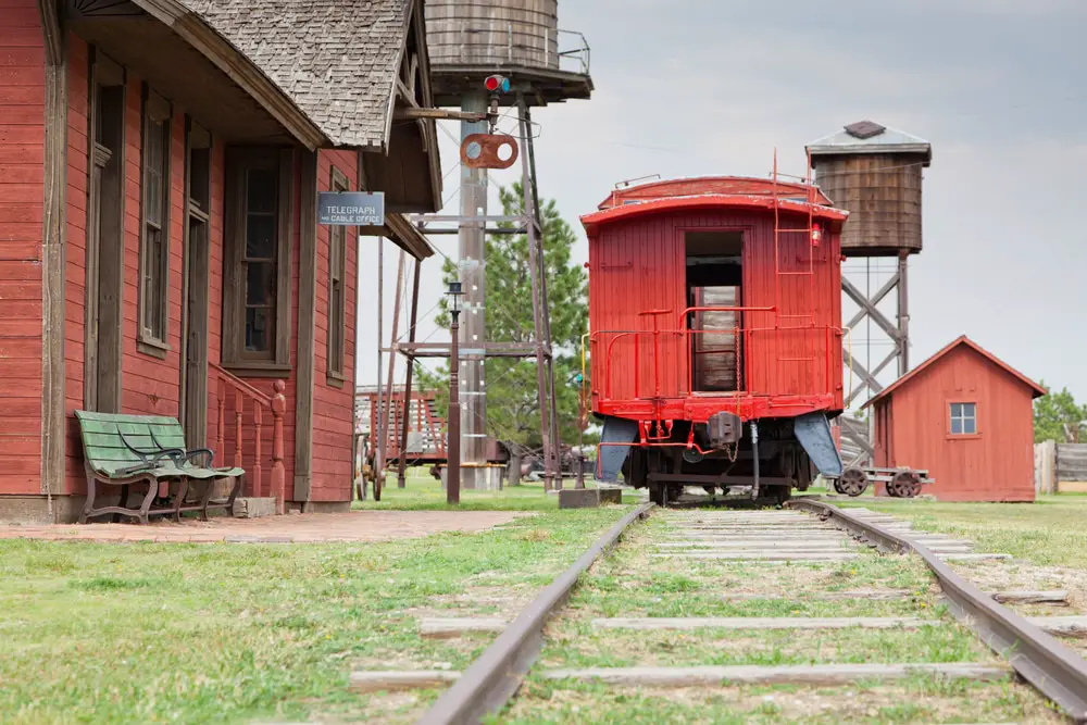 A vintage red wooden caboose sits at a old western train station as part of a historical display.